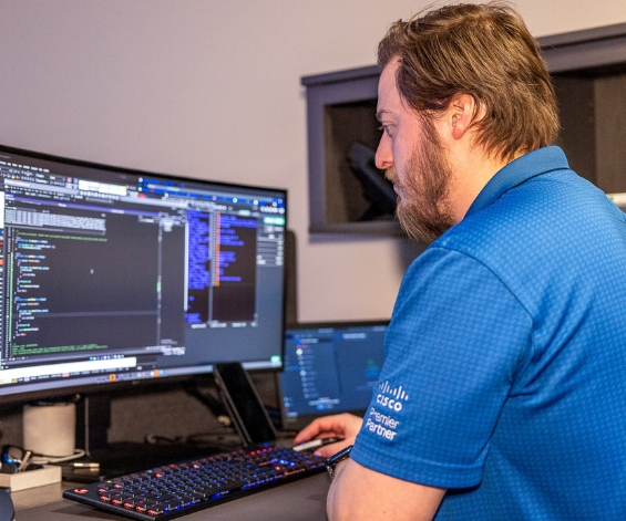 IT team member wearing blue polo shirt in front of his workstation working